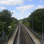 Looking down from a footbridge across railway tracks between the station platforms, the railway line stretches into the distance.