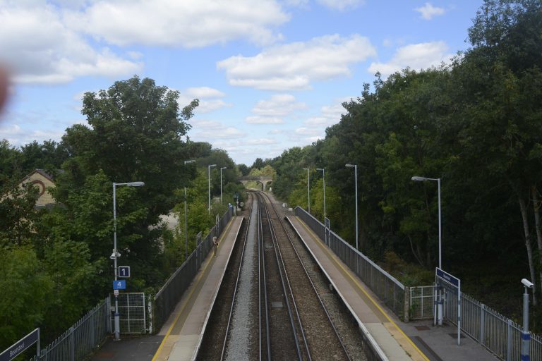 Looking down from a footbridge across railway tracks between the station platforms, the railway line stretches into the distance.