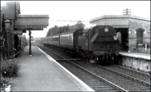 A black and white photograph of a steam engine and coaches at Harrietsham station.