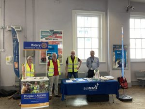 Four volunteers stood behind colourful display stalls. Brochures and posters promote rail safety.