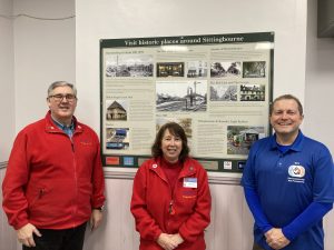 Richard Emmett (wearing red), Theresa Emmett (wearing red) and Gary Outram (wearing blue) in front of the history board.