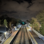 A night scene of Cuxton station from the footbride. Empty tracks between well lit platforms, a distant signal is green.