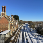 An elegant victorian station with snow covered tracks and platforms beneath a blue sky.