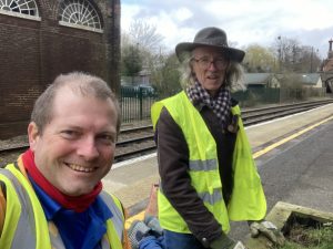 Gary and Dave in hi-vis weeding a planter on the station platform