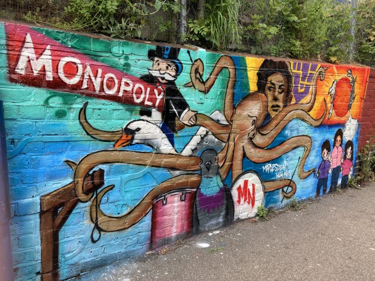 A colourful mural featuring Mr Monopoly, An Octopus, drums, a swan, a gallows and diverse people