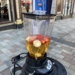 A blender on the back of a static bicycle, filled with apple juice and pieces of fruit