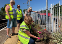 Four people tending a flowerbed on a station platform