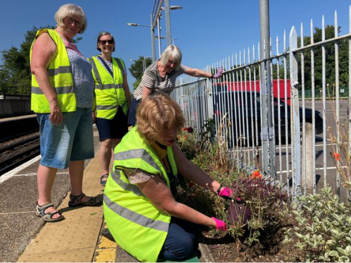 Four people tending a flowerbed on a station platform