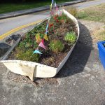 A white boat planter with colourful flowers and flags