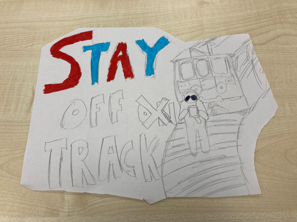 Rail safety artwotk in progress. Stay Off (On crossed out) Track with a hand drawn image of a person walking on a railway track in front of a train.