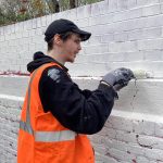 A person applies white masonry paint to a brick wall previously painted red