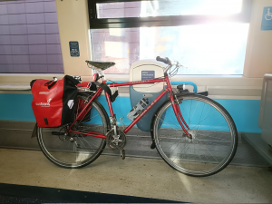 A red bicycle with panniers labelled "Sustrans" in the cycle storage area on a train.