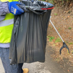 A person holding a rubbish sack and litter picker