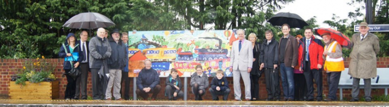 A crowd of people stood around a colourful mural on a station platform