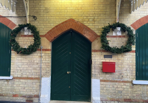 Green station entrance doors with shuttered windows either side. Two holly wreaths hang between the doors and windows