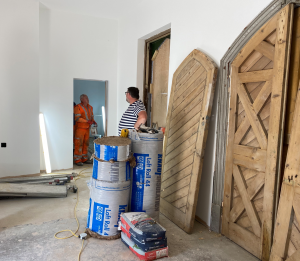 Renovations in progress. Walls are smoothly plastered, wooden doors have been stripped of their paint. Rolls of loft insulation and bags of plaster are on the floor, two workers are chatting.