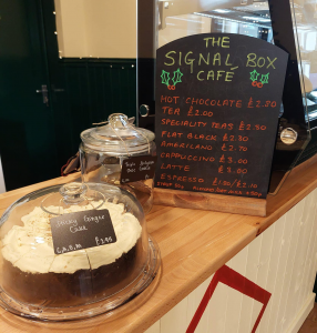 A chalk board welcoming you to the signal box cafe with cookies and cake on a counter top