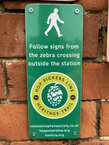 A waymarking sign for the Hop Pickers Line Heritage Trail mounted to a wall