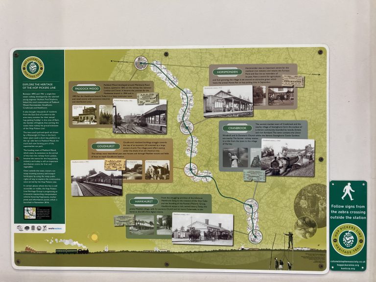 A waymarking sign for the Hop Pickers Line Heritage Trail mounted adjacent to an information panel about the line.