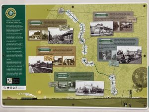 A waymarking sign for the Hop Pickers Line Heritage Trail mounted adjacent to an information panel about the line.