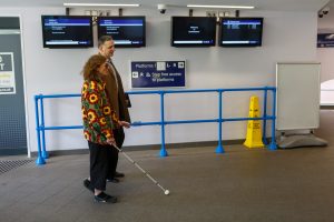 A white cane user and another person cross the station booking hall