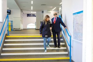 A sighted guide assists a blindfolded volunteer as they navigate a flight of stairs inside a station