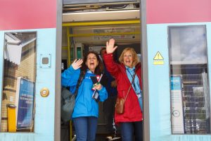Two people waving goodbye from the train as the doors close