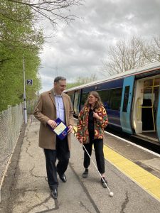 A white cane user and another person have left a train and are making their way along the platform