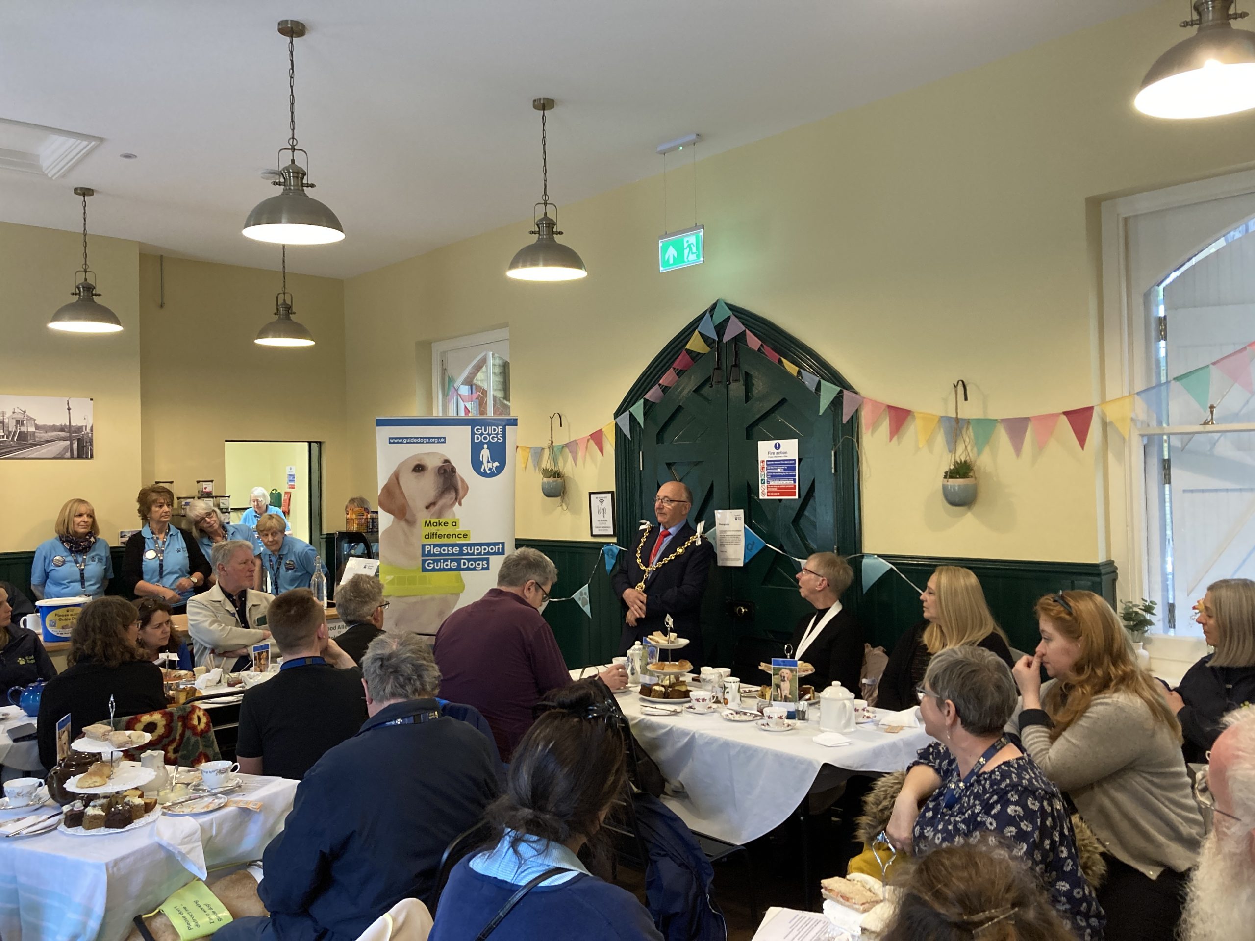 Afternoon tea st out on tables as the Mayor of Maisdstone speaks to the audience of Guide Dogs volunteers, Southeastern managers and other guests