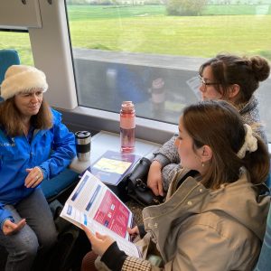 Therese discussing plans for the trip with tutors onboard the train, They are sat around a small table between rows of seats.