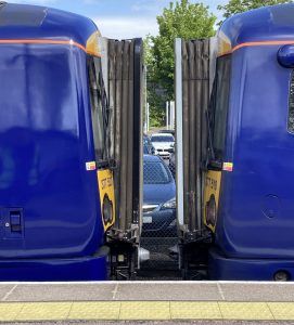Two blue liveried Southeastern trains at a station platform. The trains have just been separated, leaving a 0.5m gap between them through which cars can be seen in the station car park