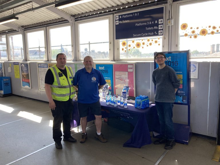 A member of Southeastern staff, Gary and Dominic at a promotional stall. The stall is flanked by posters promoting the British Transport Police 61016 SMS service.