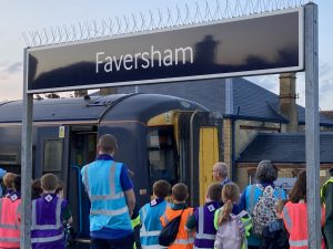 A group of children in hi-vis jackets on the platform at Faversham station. They are looking at a train.