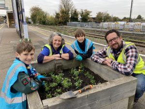 Cubs and cub leaders admiring their hard work planting new flowers into a wooden planter on the platform