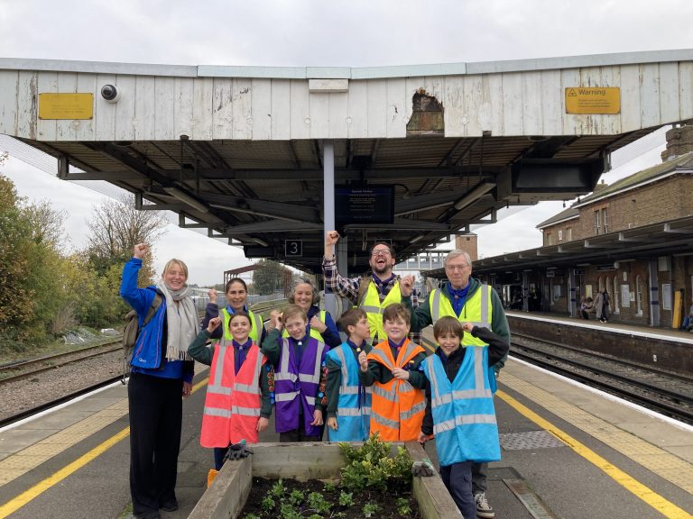 Vicky, Cub leaders, helpers and the Cubs stand on the platform behind a planter they have filled with flowers and bulbs