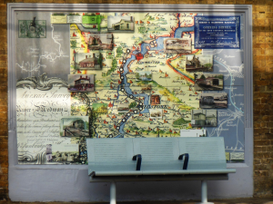 A mural on a wall behind a bench on a station platform. The mural depicts a historical map of the Medway Valley Line and surrounding area
