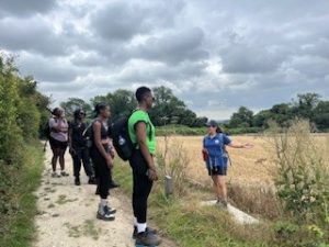 Therese stands at the edge of the path, with a field of wheat behind her. She is talking to a group of walkers spread along the path