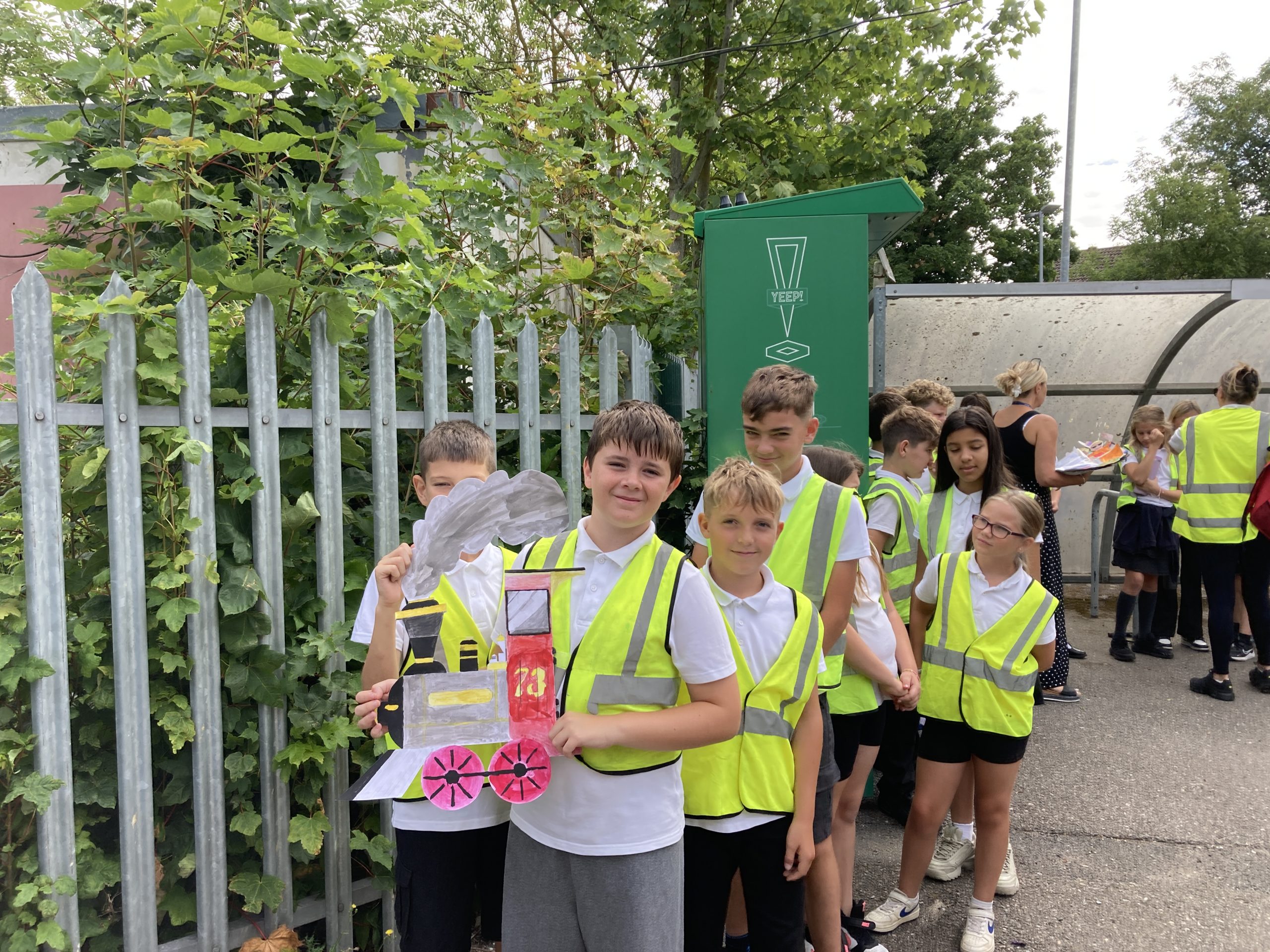 Young learners in hi-vis jackets show off their drawing of a train as they wait for the procession to begin.