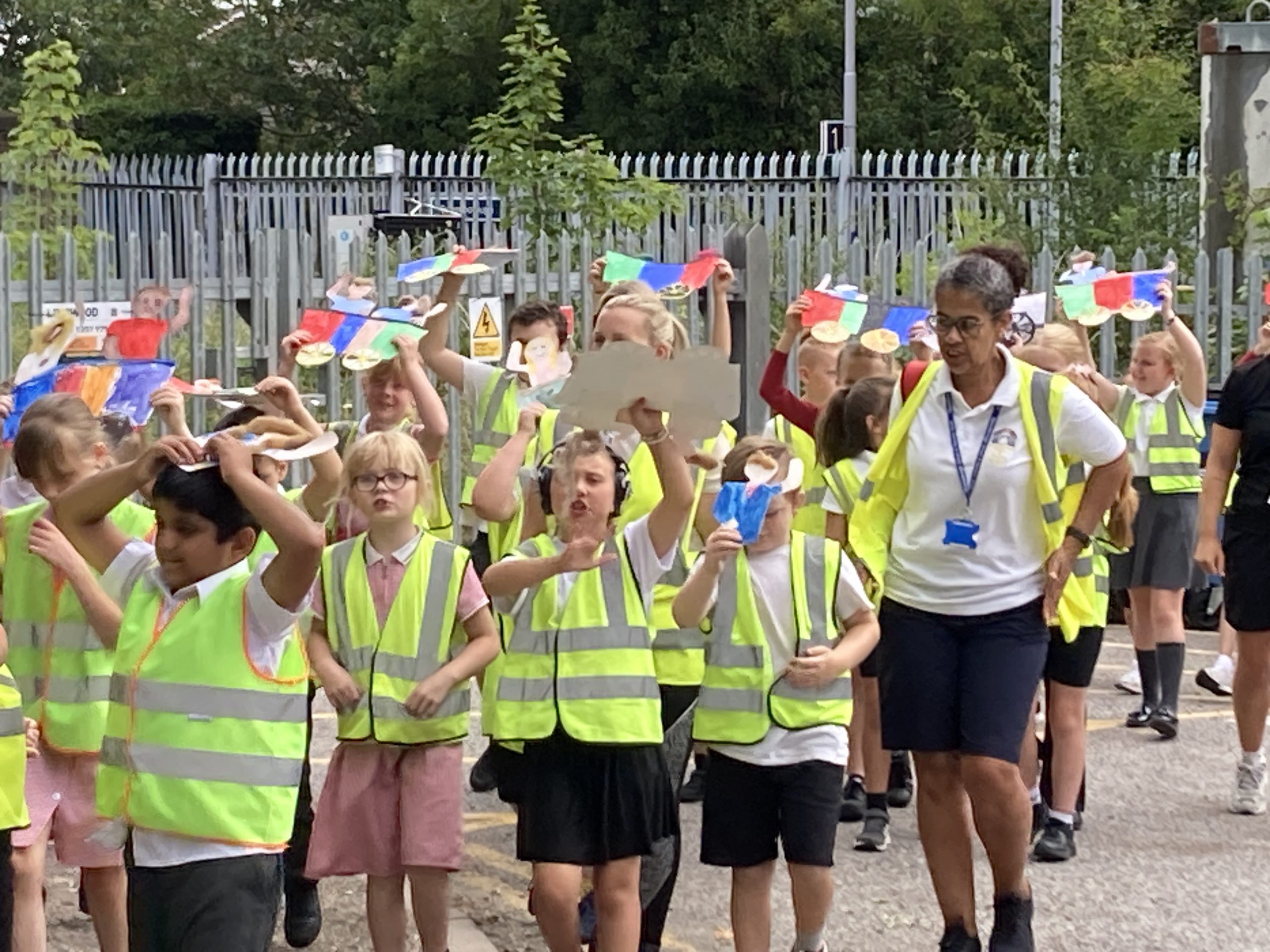 Young learners in hi-vis jackets raise their drawings of train carriages above their heads as the procession begins.
