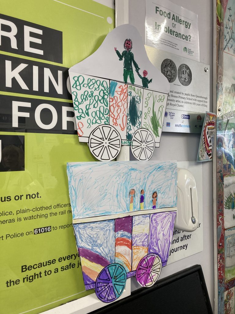 Two decorated railway carriages with passengers pinned to the wall in Queenborough station's ticket office.