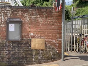 A cardboard sheet attached to brickwork. The picture is to illustrate the potential to place a heritage rail crossing sign at the location, it has no aesthetic value