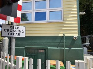 View of a signal box with a wooden door to a basement area, surrounded by wheelie bins of a signal box. The picture is to illustrate the potential to place a heritage rail crossing sign at the location, it has no aesthetic value