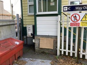 A cardboard sheet attached to the brickwork of a signal box. The picture is to illustrate the potential to place a heritage rail crossing sign at the location, it has no aesthetic value