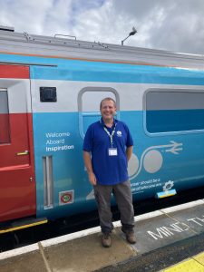 Gary poses for a photo outside of the Inspiration train. A sign reads "Welcome Aboard Inspiration"