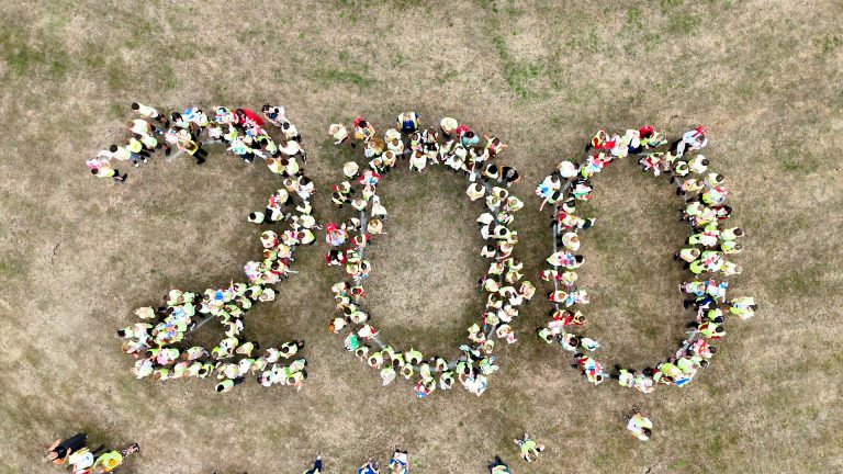 Drone image of around 180 young learners and their tutors forming "200" on the town green.