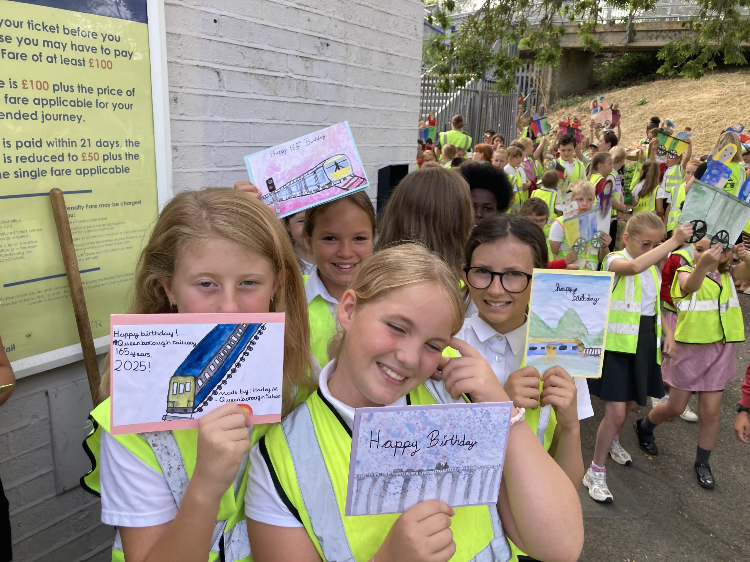 Young learners in hi-vis jackets display birthday cards they have created to celebrate Queenborough station's birthday