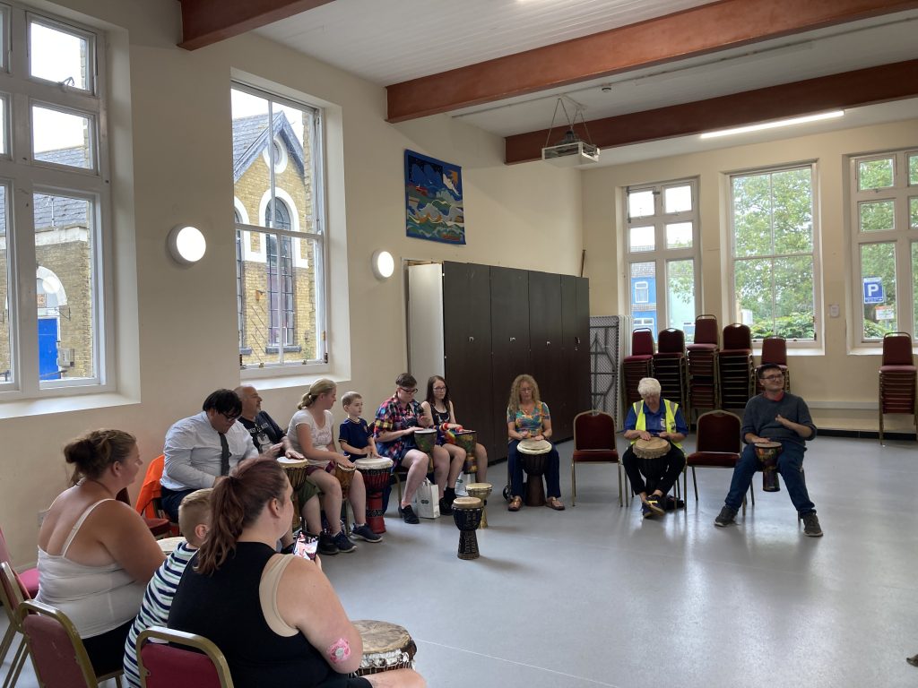 A group of people seated in a semi-circle playing African drums in a hall.