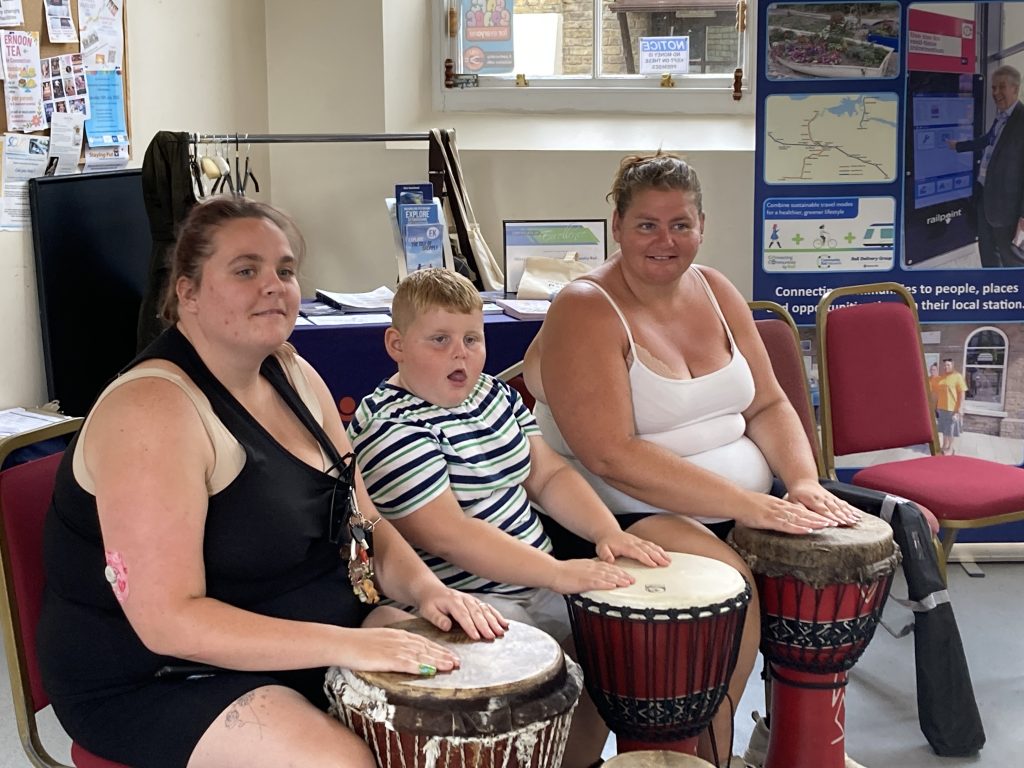 Three people seated in a hall playing African drums
