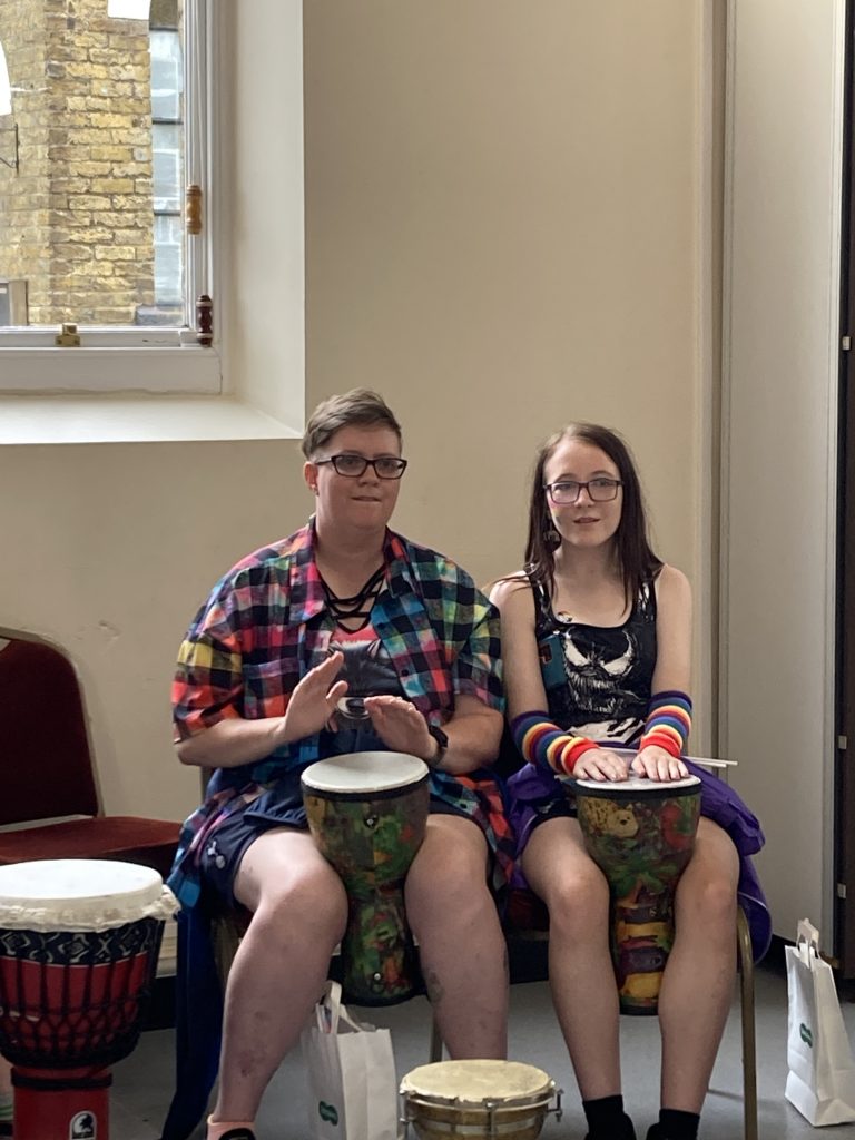 Two people seated in a hall playing African drums