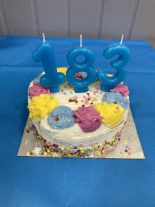 A colourful cake with number candles, 183. The cake is on a silver base